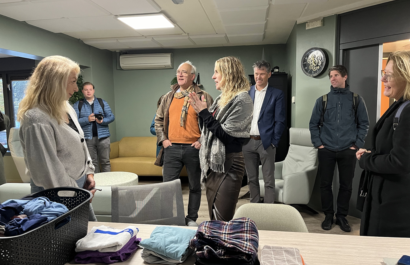 Staatssecretaris Maeijer staat in een ruimte te praten met diverse mensen met schone kleding op de tafel